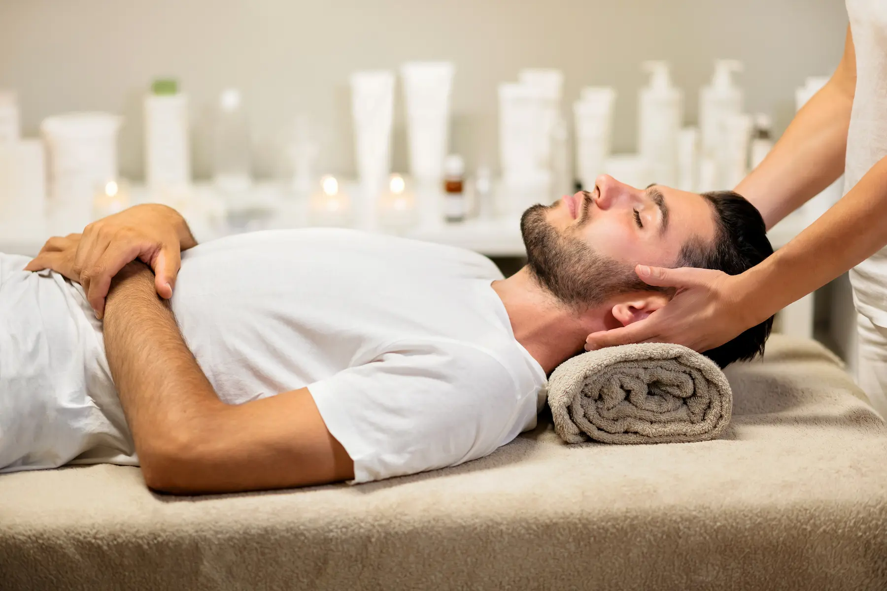 Uomo disteso su lettino spa mentre riceve un massaggio al collo