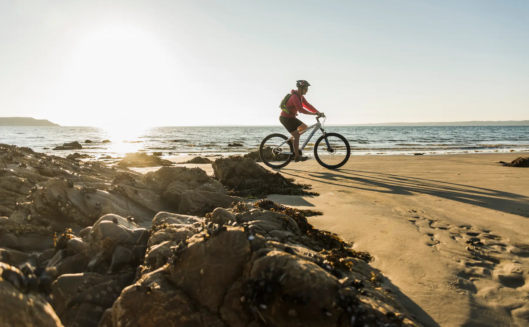 Uomo che pedala su una bici da spiaggia sulla sabbia al tramonto, con il mare sullo sfondo